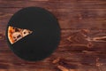 One slices of delicious pizza with ham, mozzarella, mushrooms and olives on a slate black platter which is on wooden table Royalty Free Stock Photo
