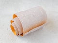 One small roll of extra coarse aluminum oxide sandpaper on a white rough textured background. Abrasive paper for dry sanding.