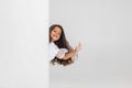 One smiling little cute Caucasian girl peeking around the corner over white studio background.