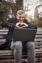 One smiling young man, sitting on bench in public park using laptop, Royalty Free Stock Photo