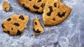 One soft freshly baked chocolate chip cookie with crumbs and chunks on a gray marble kitchen countertop. American traditional