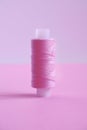 One spool of sewing thread lilac pink, violet, crimson on a pink backgroun.