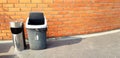 One stainless steel and Black plastic garbage putting on street with brown brick wall for people dumping trash, dross or refuse