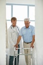 One step at a time...a male doctor assisting his senior patient whos using a walker for support.
