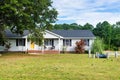 One story small residential home with board siding on the facade. With a large lawn and a tree