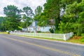 One-story small residential home by the road with board siding on the facade. With a low fence, a lawn and coniferous trees Royalty Free Stock Photo