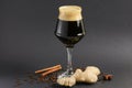 One tall glass of cold dark craft beer with spices over black background. Hops, anise, cinnamon, ginger. Copy space Royalty Free Stock Photo