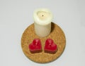 One tall white and two heart shaped red candles on round cork hot pad on white background. Royalty Free Stock Photo