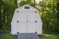 One tan shed in the backyard surrounded by multiple green trees