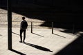 One teenage boy standing alone waiting for a tram on bus stop in sunlight, with shadows