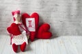 One tilde doll in a red dress, and a white apron, and in a red kalpak sits on a light background with red textile hearts. Interior