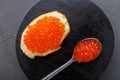 One toast with butter and red caviar next to a spoon with caviar on a wooden board on a concrete background. Royalty Free Stock Photo