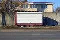 One trailer with white shutters on wheels stands on the street near a gray fence Royalty Free Stock Photo