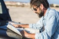 One traveler man looking paper guide map on car hood outside to find best roads and arrival destination. Transport and travel with Royalty Free Stock Photo