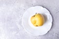 One ugly yellow apple on white figured plate on grey concrete background.