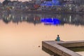 One unrecognizable person meditating on the lake bank at Pushkar, Rajasthan, India. Temples, buildings and ghats reflecting on the