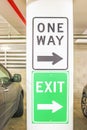 One way and exit signs on pillar in parking garage with parked cars to either side - close-up an selective focus