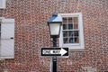 One way sign hanging on a black pole with street lamp, with a traditional brick wall on the back Royalty Free Stock Photo