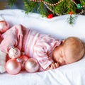 One week old newborn baby with pink balls near Christmas tree with colorful garland lights on background. Closeup of Royalty Free Stock Photo