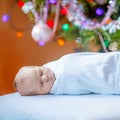 One week old newborn baby wrapped in blanket near Christmas tree with colorful garland lights on background. Closeup of Royalty Free Stock Photo