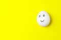 One white chicken egg with smiling face on yellow background with copy space Royalty Free Stock Photo