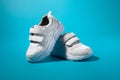 one white children's running shoe stands on the back of another running shoe on a blue paper background with a hard Royalty Free Stock Photo