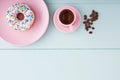 One white donut or doughnut in a pink plate, cappuccino in a pink coffee cup and coffee beans on blue wooden table Royalty Free Stock Photo