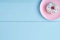 One white donut or doughnut in a pink plate on a pastel blue wooden table background with copy space