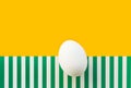One white egg on duotone yellow green striped background imitating grass. Easter concept. Trendy minimalist shabby chic style