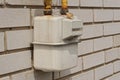 One White Metal Gas Meter With Yellow Iron Pipes On A Gray Brick Wall
