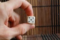 One white plastic dices in man`s hand on brown wooden table background. Six sides cube with black dots. Number 5