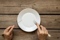 One white plate and fork with a knife in hands on an old wooden table in the kitchen at home, restaurant business Royalty Free Stock Photo