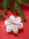 One white scented candle in the shape of a snowflake and a fir branch on a red background