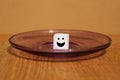 One white sugar cube with a cheerful face painted on a stained plate, concept of excessive sugar intake, diabetic, close-up, copy