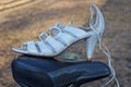 one white womens leather high heel sandal standing on a black bicycle saddle