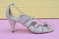 one white womens leather high heel sandal stands on a pink wooden table