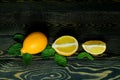 One whole bright yellow lemon and two halves of lemon with mint leaves laid out on a coarse wooden authentic background Royalty Free Stock Photo