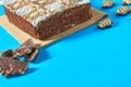 One whole checkered rectangular cake on bamboo mat near candy and broken chocolate bar with nuts lies on blue table on party