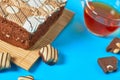 One whole checkered rectangular cake near broken chocolate bar, candy and full glass cup of tea lies on blue table on party Royalty Free Stock Photo