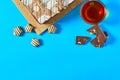 One whole checkered rectangular cake near broken chocolate bar, candy and full glass cup of tea lies on blue table on party Royalty Free Stock Photo