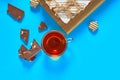 One whole checkered rectangular cake near broken chocolate bar, candy and full glass cup of tea lies on blue table on party Royalty Free Stock Photo