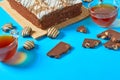 One whole checkered rectangular cake near broken chocolate bar, candy and two full glass cups of tea lies on blue table on party Royalty Free Stock Photo