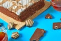 One whole checkered rectangular cake near broken chocolate bar, candy and two full glass cups of tea lies on blue table on party