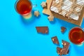 One whole checkered rectangular cake near broken chocolate bar, candy and two full glass cups of tea lies on blue table on party