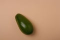 One whole green fresh avocado on beige background. Minimal styled composition