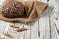 One whole loaf of rye bread with seeds of sunflower near sackcloth and spikelets of wheat lies on weathered white wooden table