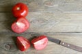 One whole and several cut tomatoes red, kitchen knife, close-up isolated on brown wood backgroun Royalty Free Stock Photo