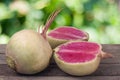 One whole and sliced watermelon radish on a wooden table with blurred garden background Royalty Free Stock Photo