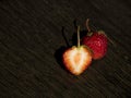 One whole strawberry and one half strawberry on a dark wooden surface Royalty Free Stock Photo