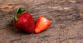 One whole strawberry and one half strawberry on a dark wooden surface with space to write on the right Royalty Free Stock Photo